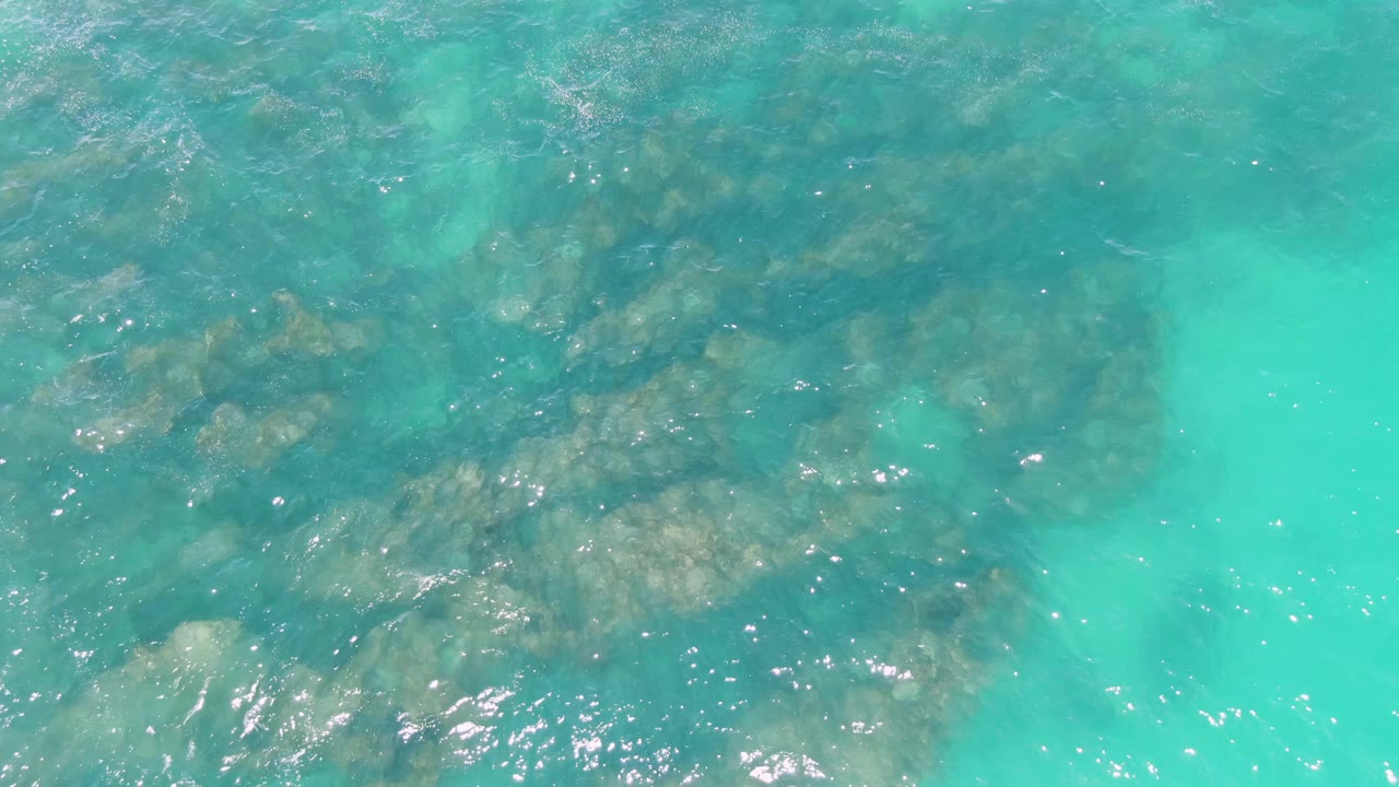 Straight-down frame over Buzzards Beach water with clustered submerged rocks, pale turquoise edges, and no visible people.