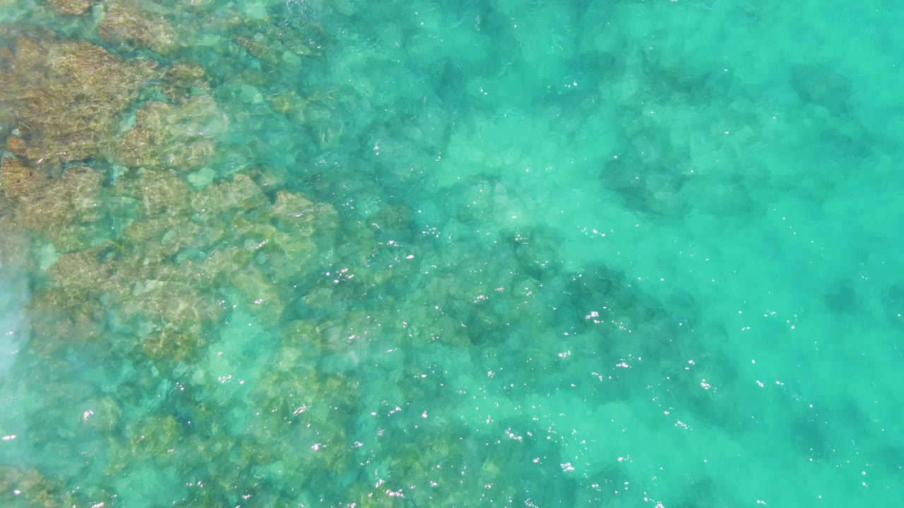 Clear shallow ocean at Buzzards Beach, Baja California Sur, with reef-like rock patches concentrated on the left and center and no visible people.