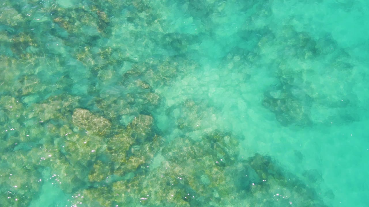Clear shallow water at Buzzards Beach, Baja California Sur, with a denser patch of submerged rocks toward the left and no visible people.