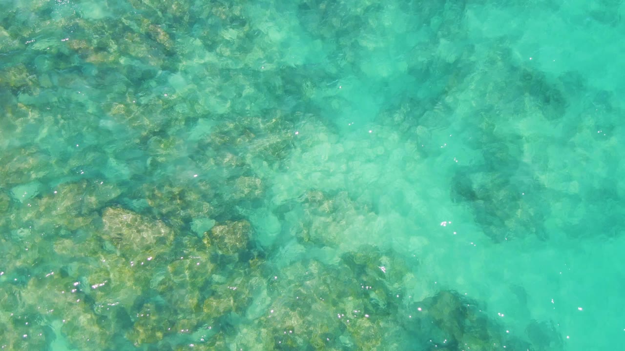 Turquoise water over uneven submerged rocks at Buzzards Beach, Baja California Sur, with small surface sparkles and no visible people.