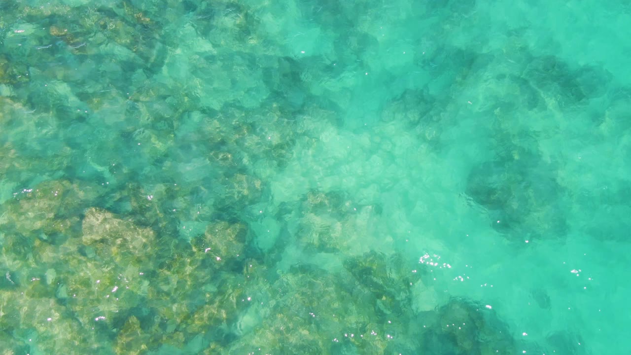 Shallow turquoise ocean with rocks and cloudy water patterns