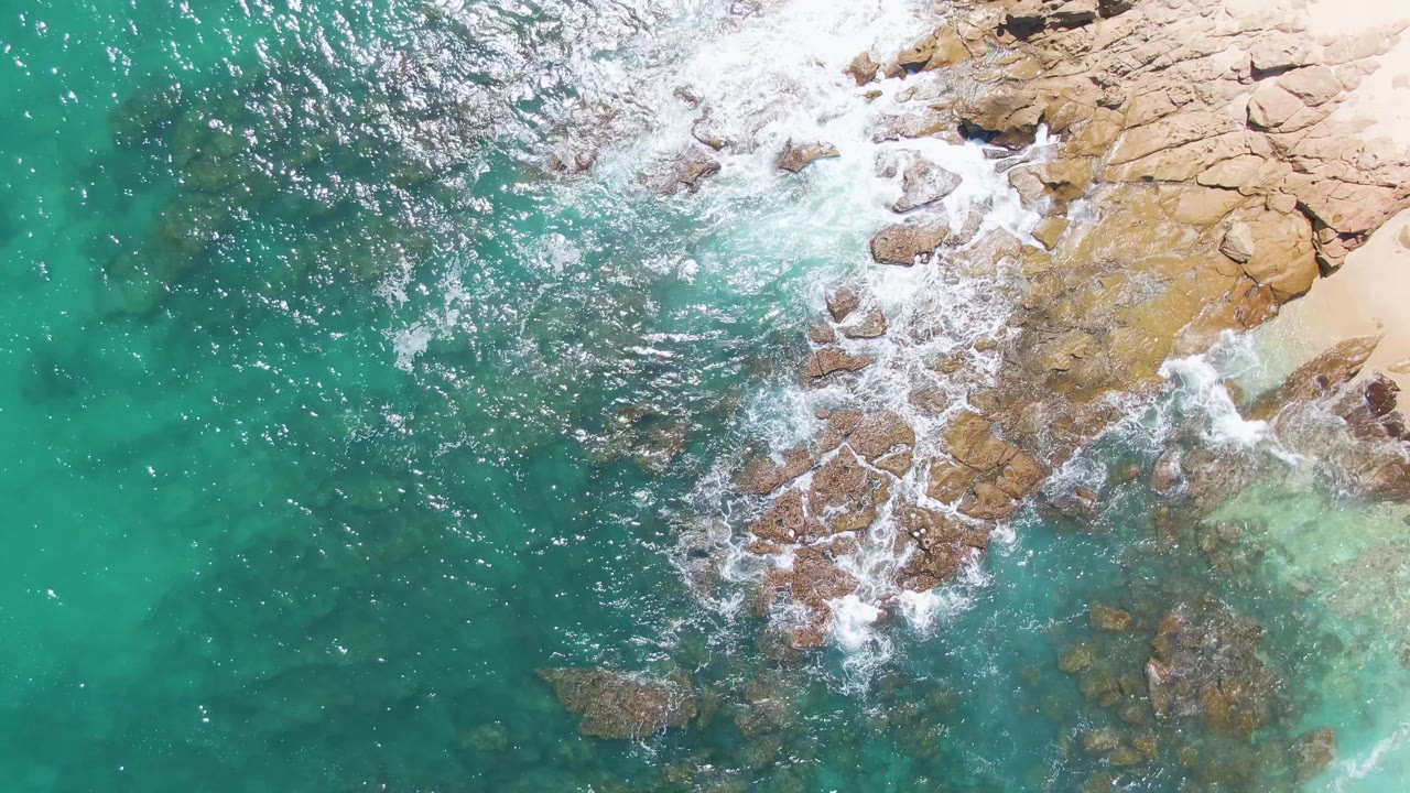 Turquoise ocean breaking over rocks beside pale sand
