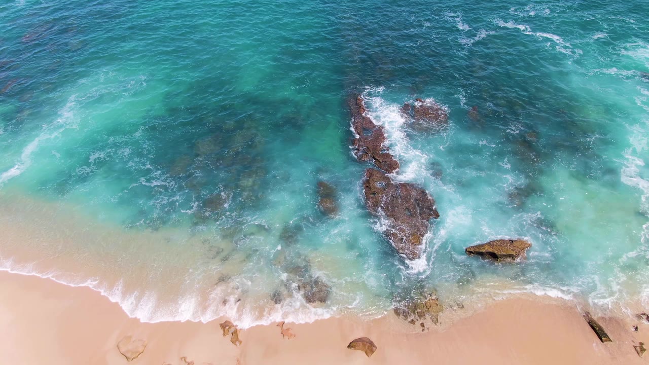 Top-down turquoise waves washing over rocks and pale sand