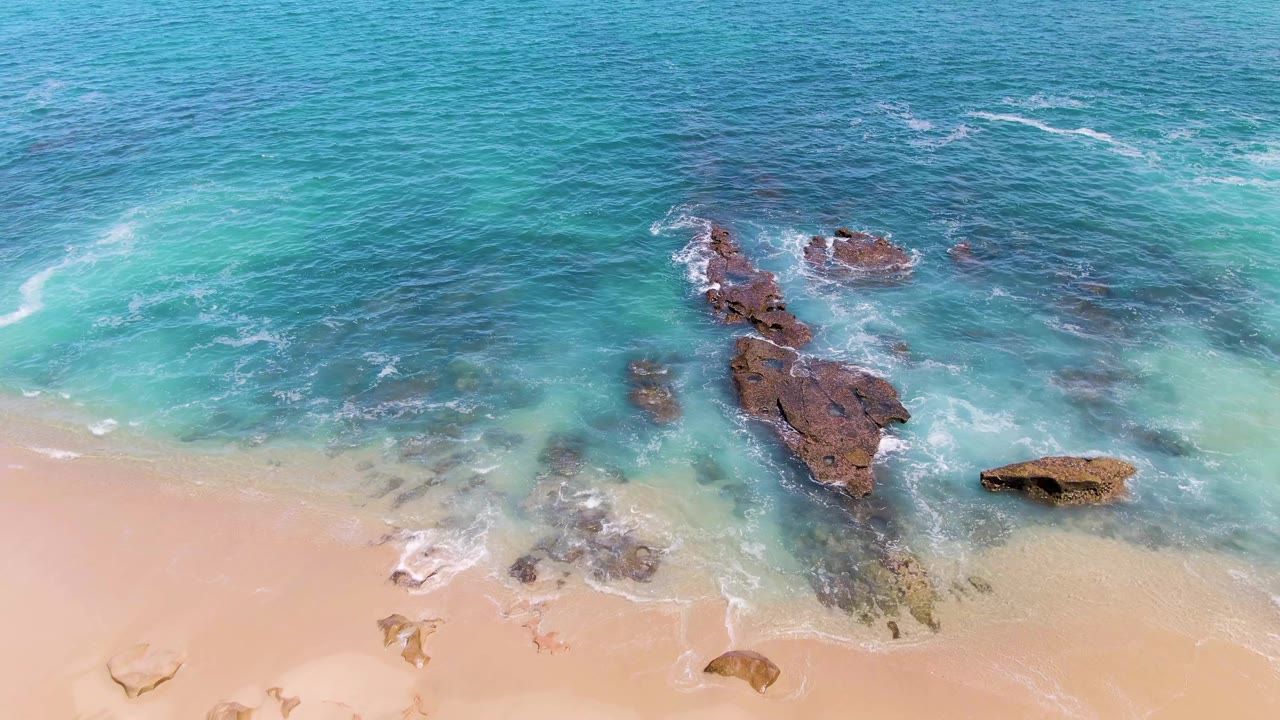Foamy wave line moving over rocks beside a sandy beach