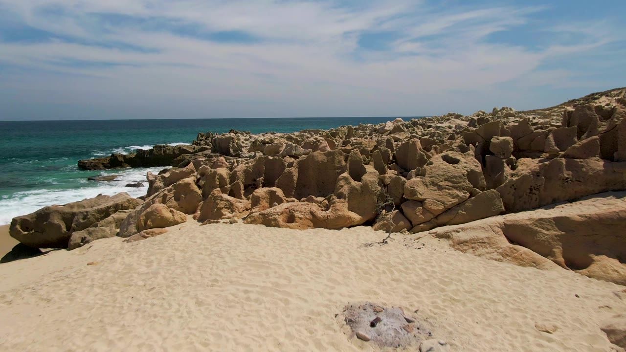 Forward beach view toward coastal rocks with ocean surf at left.