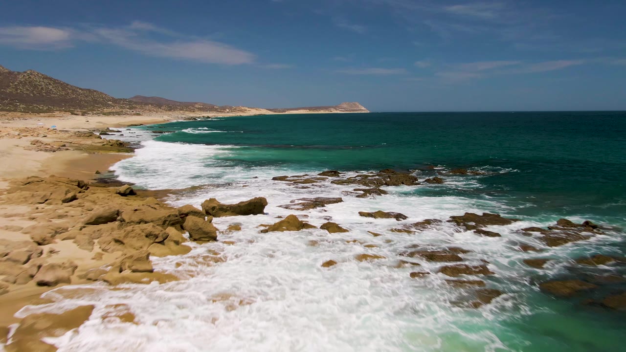Aerial coastline view with white waves over rocks and sand.