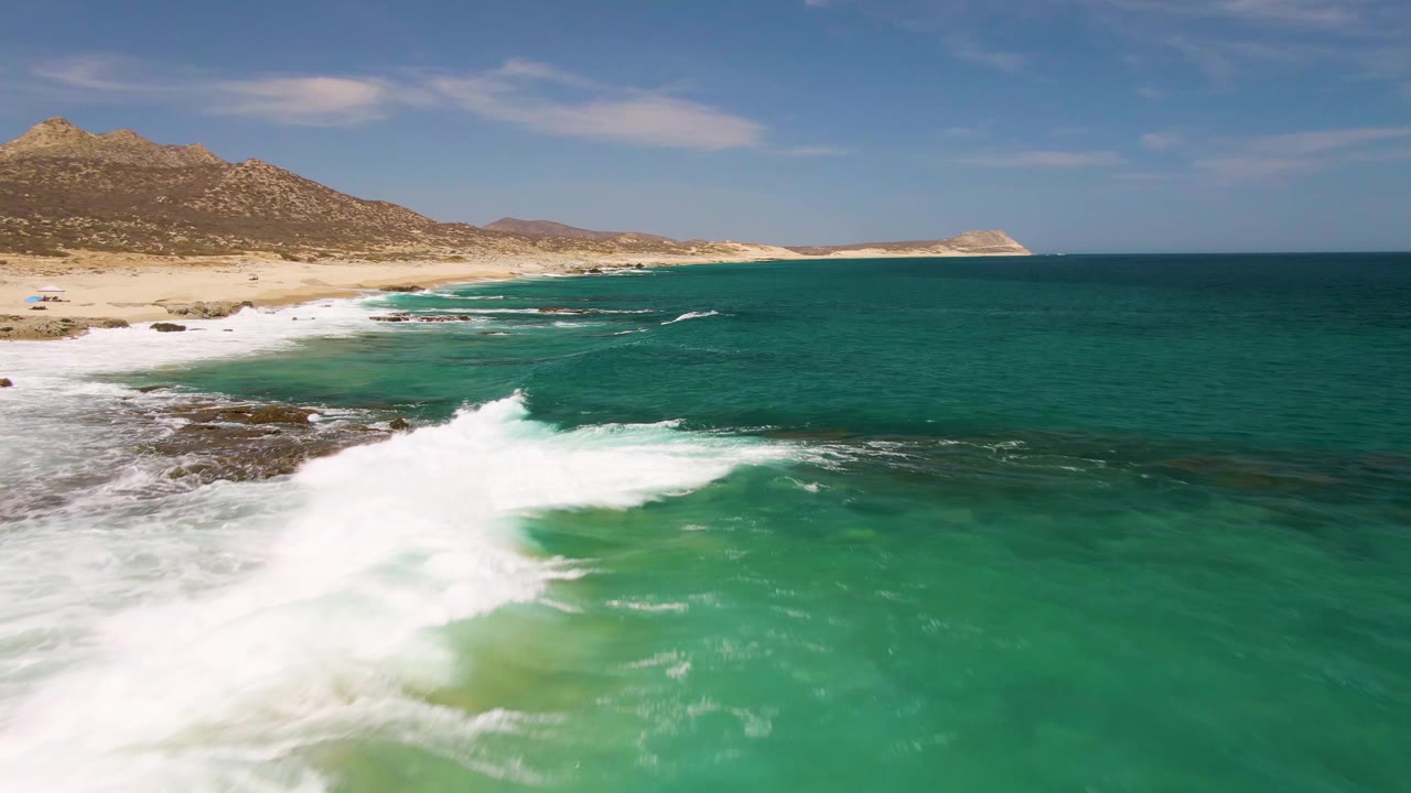 Turquoise waves breaking along a sandy coast with hills behind