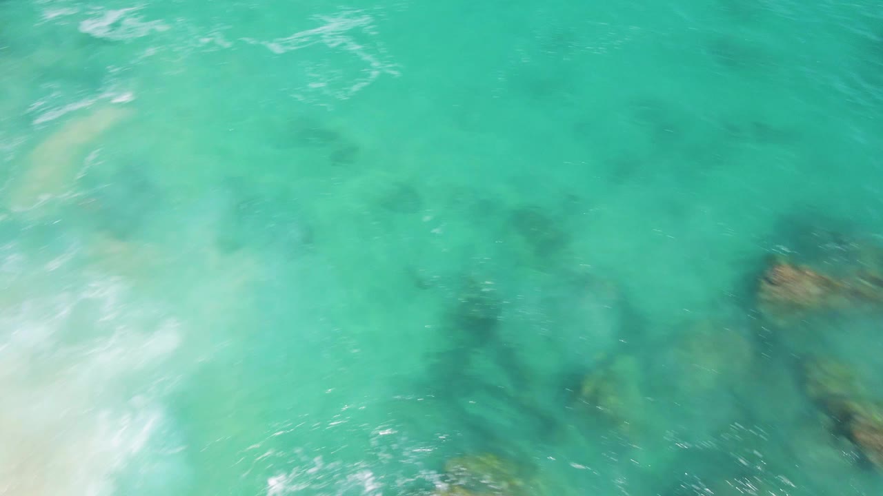 Turquoise ocean water with submerged rocks and light foam.