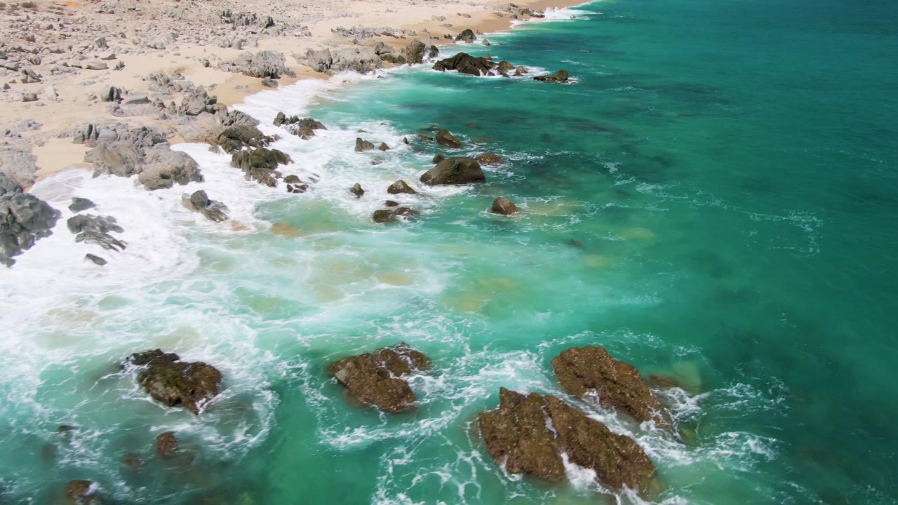 White foam spreads across shallow turquoise water around shoreline rocks.