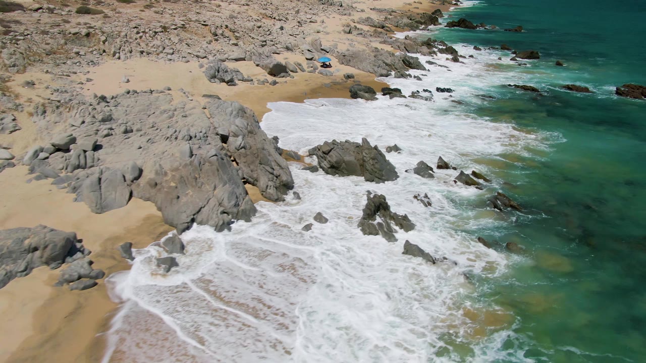 Aerial shoreline with waves receding across wet sand and rocks