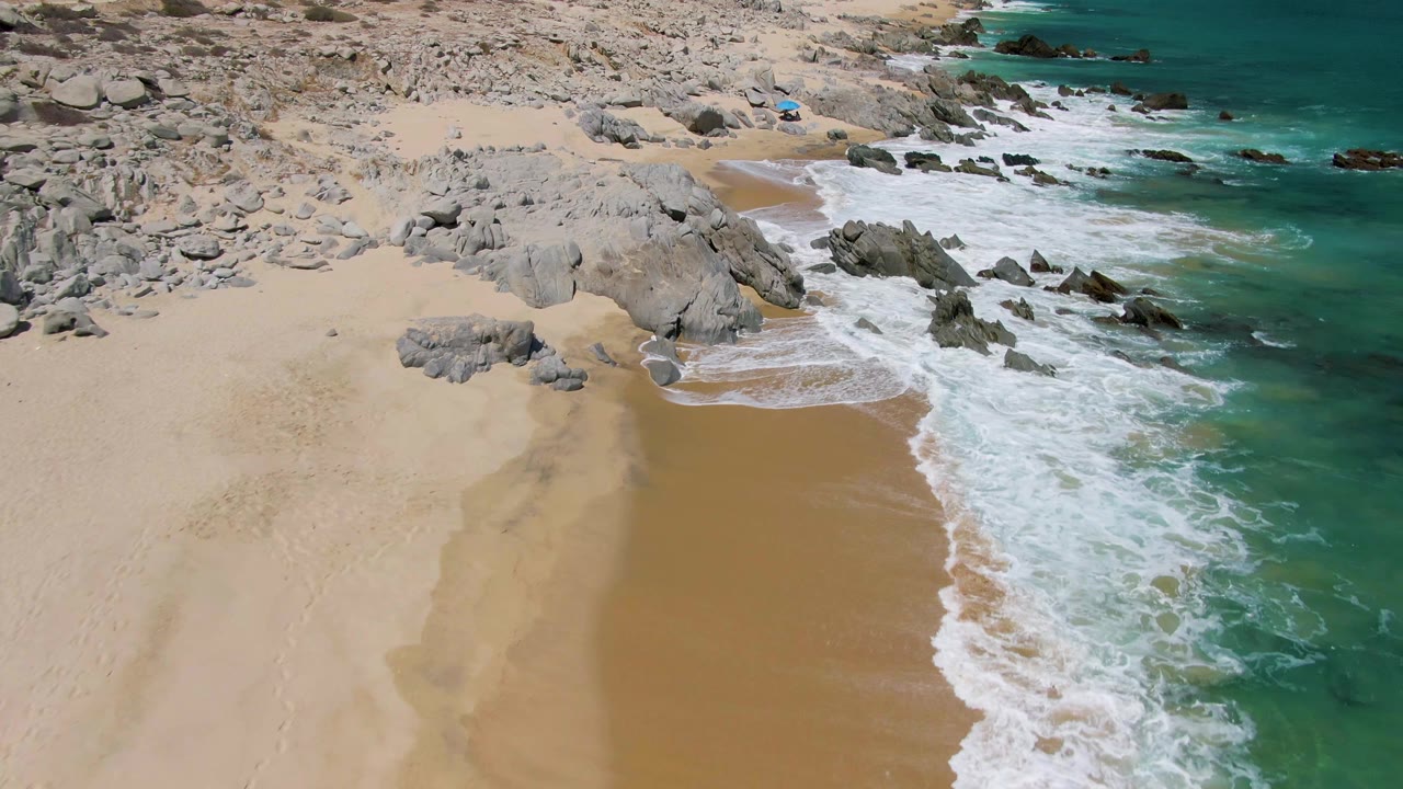 Aerial view of waves reaching a sandy beach beside gray rocks.