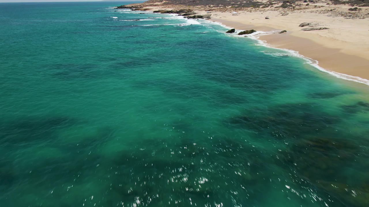 Aerial view of clear ocean water and sandy shoreline with rocks near the surf.