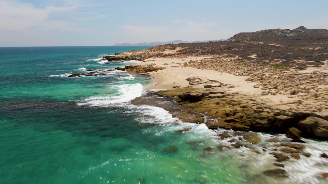 Aerial view of turquoise surf breaking on rocks beside a sandy beach.
