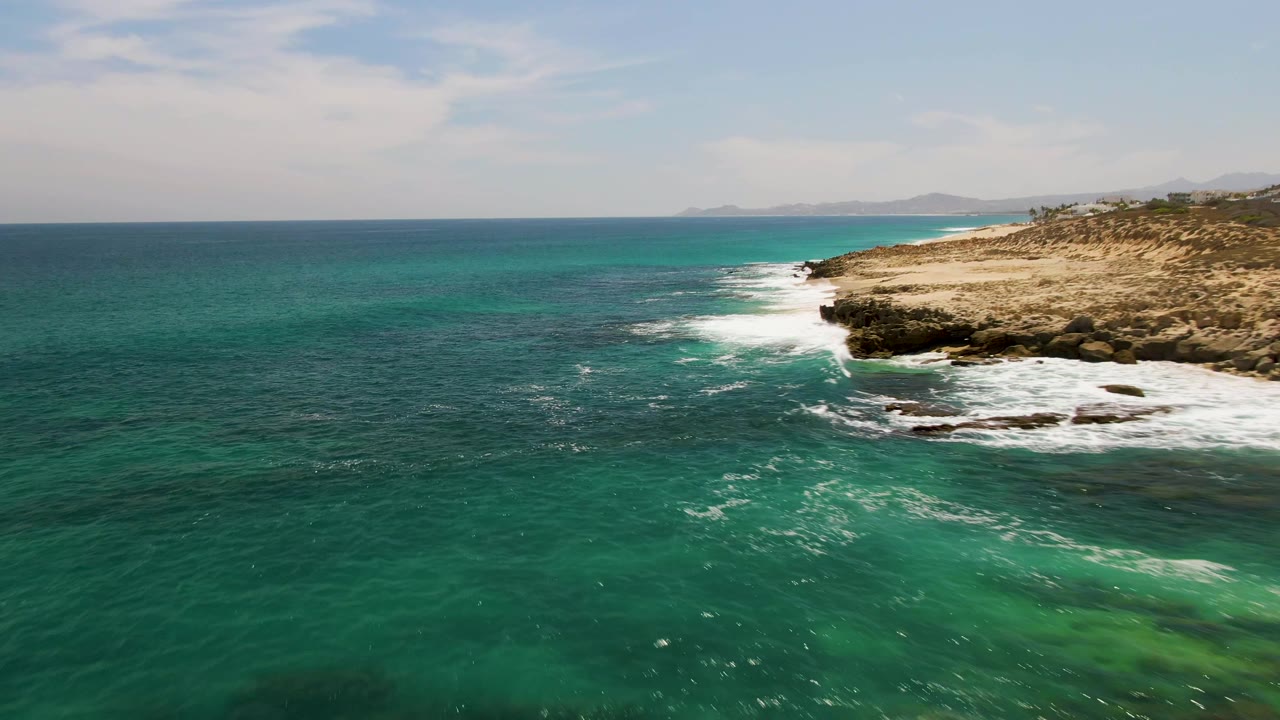 Aerial view of turquoise ocean breaking against a rocky tan shoreline.