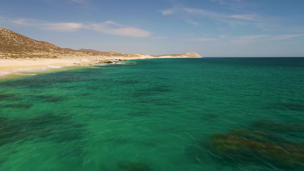 Turquoise ocean beside a sandy beach and rocky hills