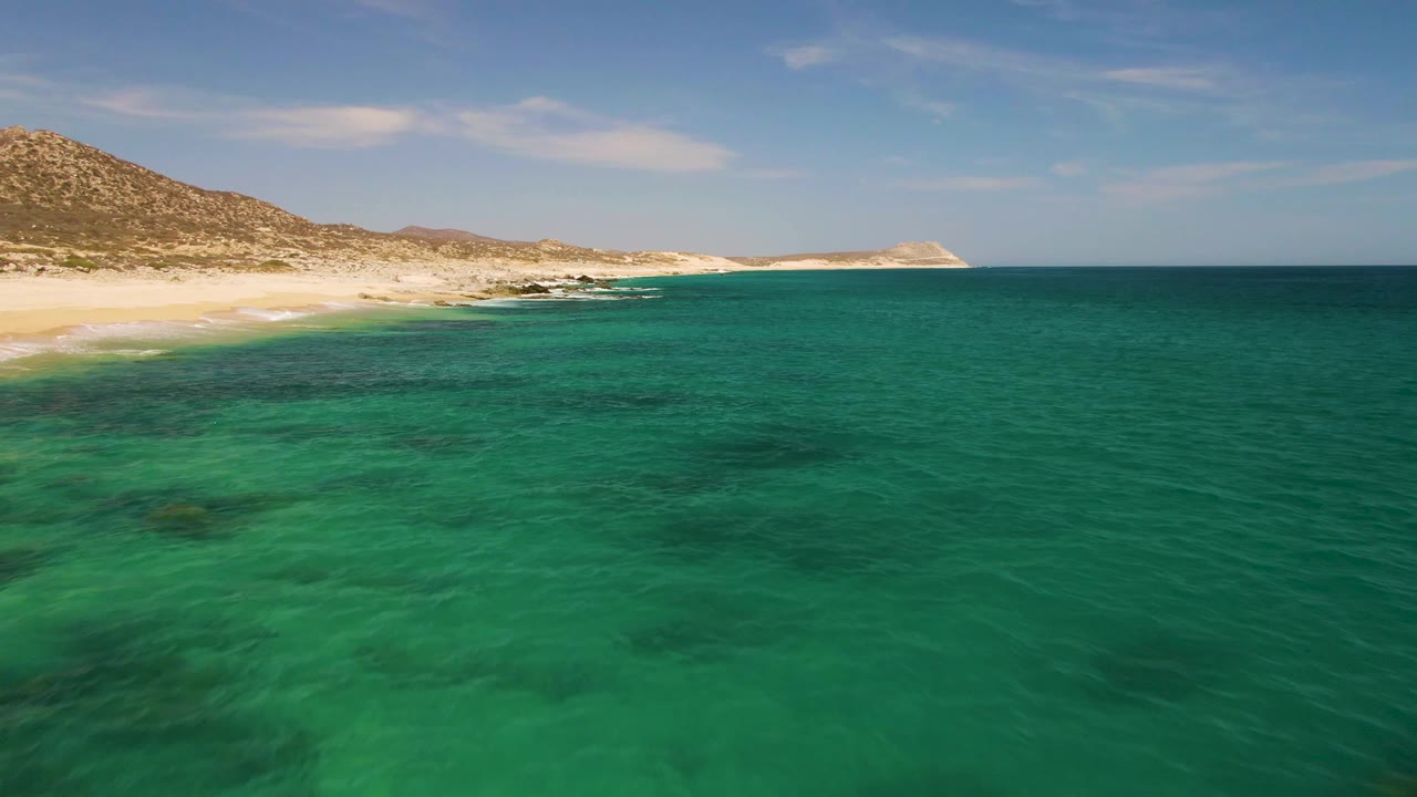 Clear turquoise ocean fills the foreground at Buzzards Beach while the sandy shore and rocky coastline stretch across the background, with no visible people.