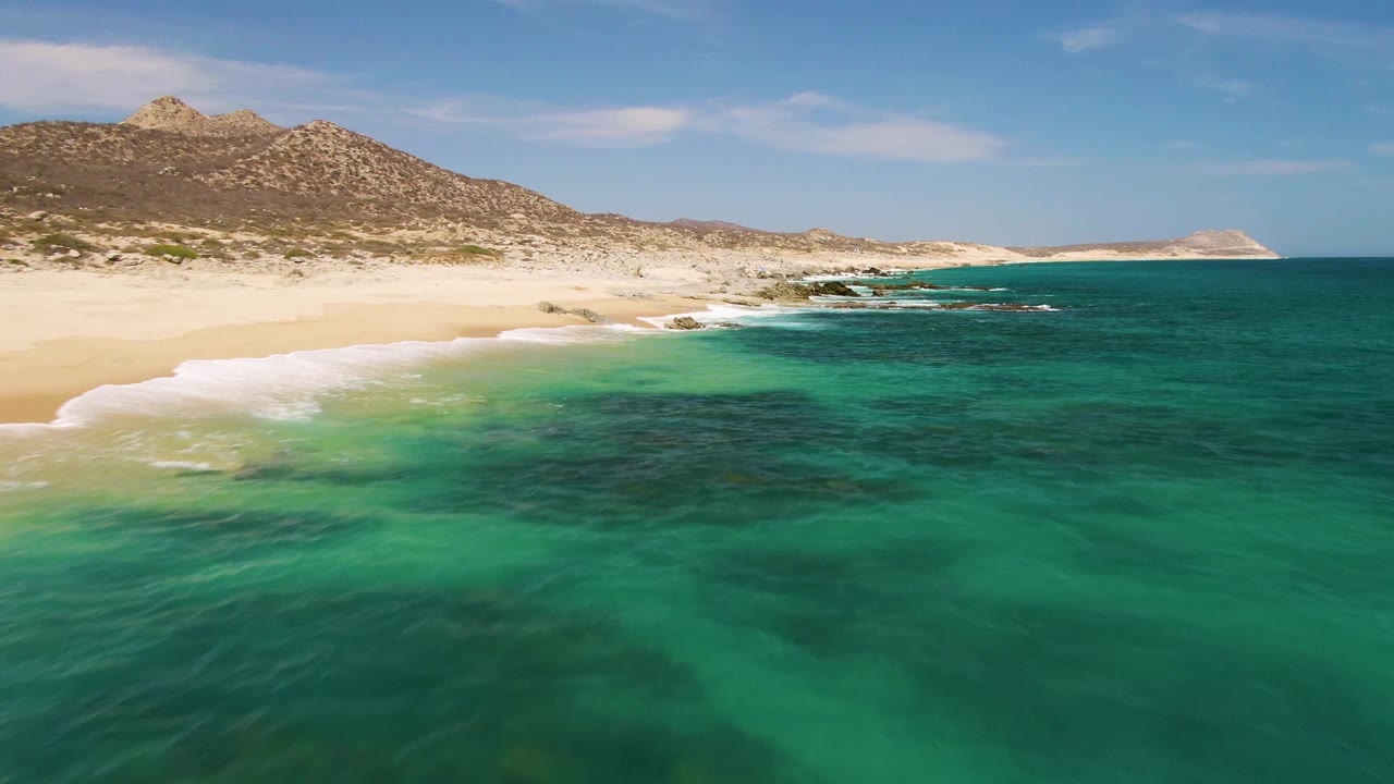 Turquoise ocean water beside a sandy beach and rocky hills