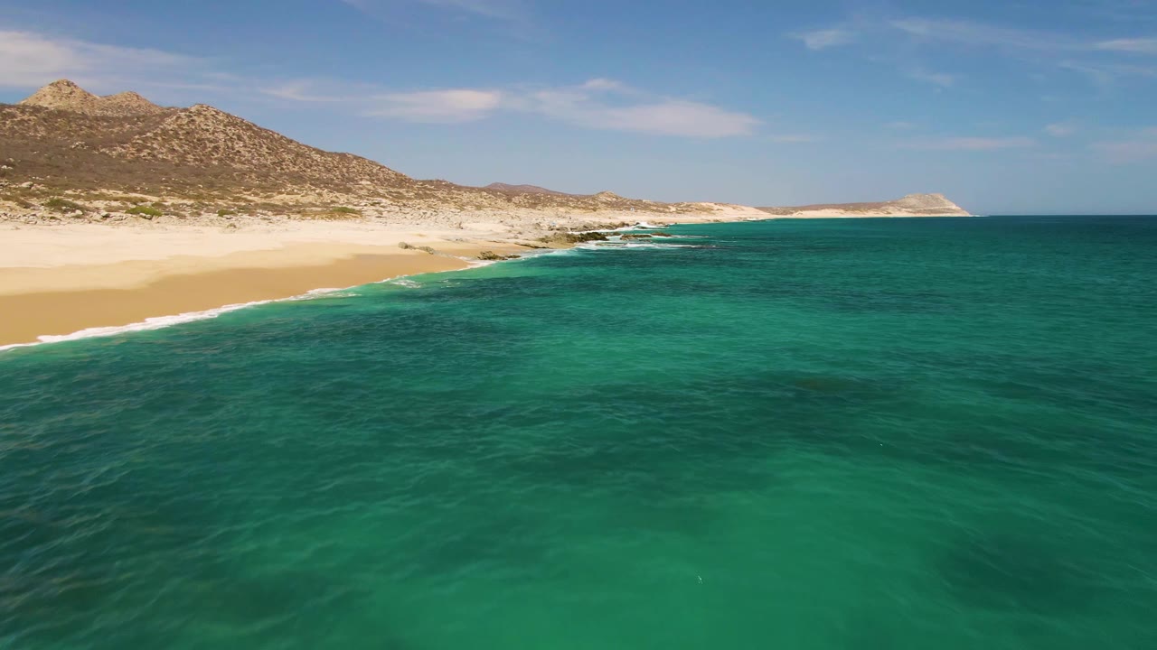 At 0:02, the Buzzards Beach shoreline remains high in frame while darker patches show through the turquoise water and no visible people appear on the sand or in the ocean.