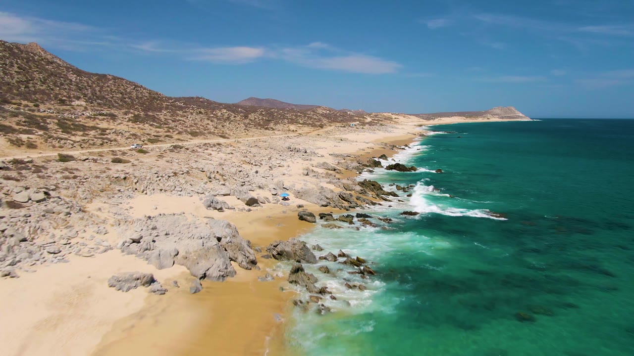 Aerial view of rocky sand beach beside turquoise ocean waves
