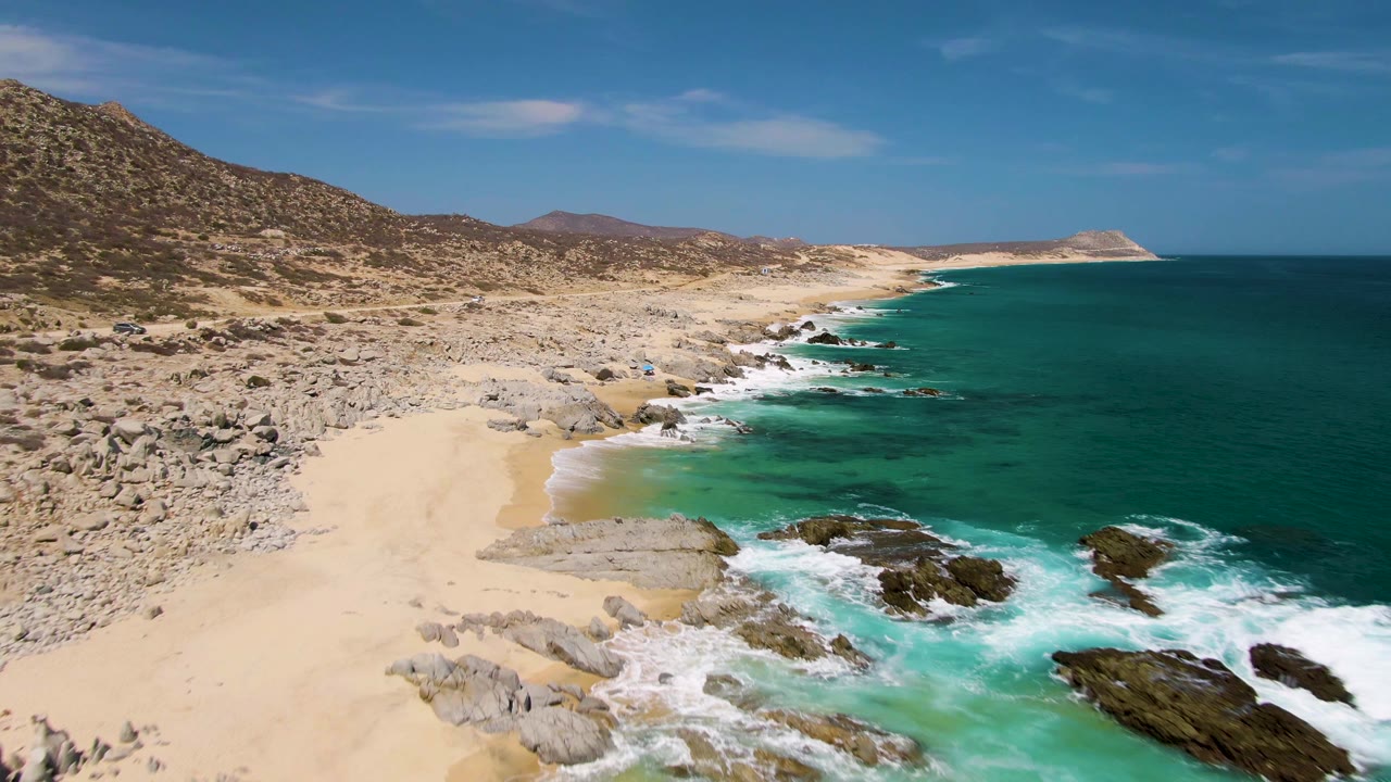 Aerial view of sandy beach, rocky shoreline, turquoise surf, and blue ocean.