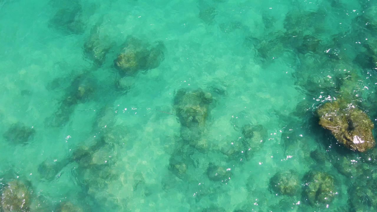 Overhead view of clear turquoise water at Buzzards Beach, Baja California Sur, with scattered submerged rocks and no visible people.