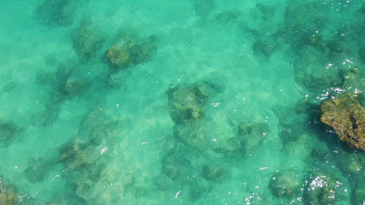Clear green-blue ocean water at Buzzards Beach shows darker submerged rocks under light ripples, with no visible people.