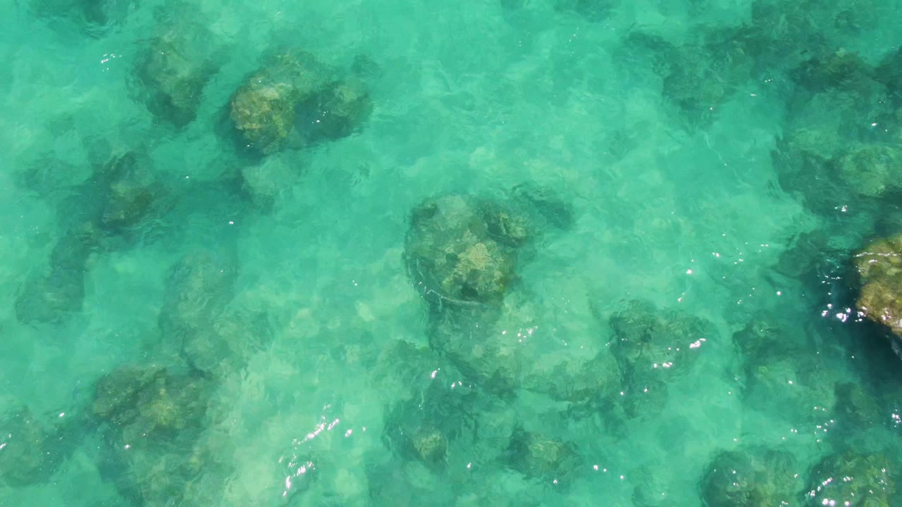 Shallow turquoise water at Buzzards Beach covers scattered underwater rocks and pale seabed areas, with no swimmers or people visible.