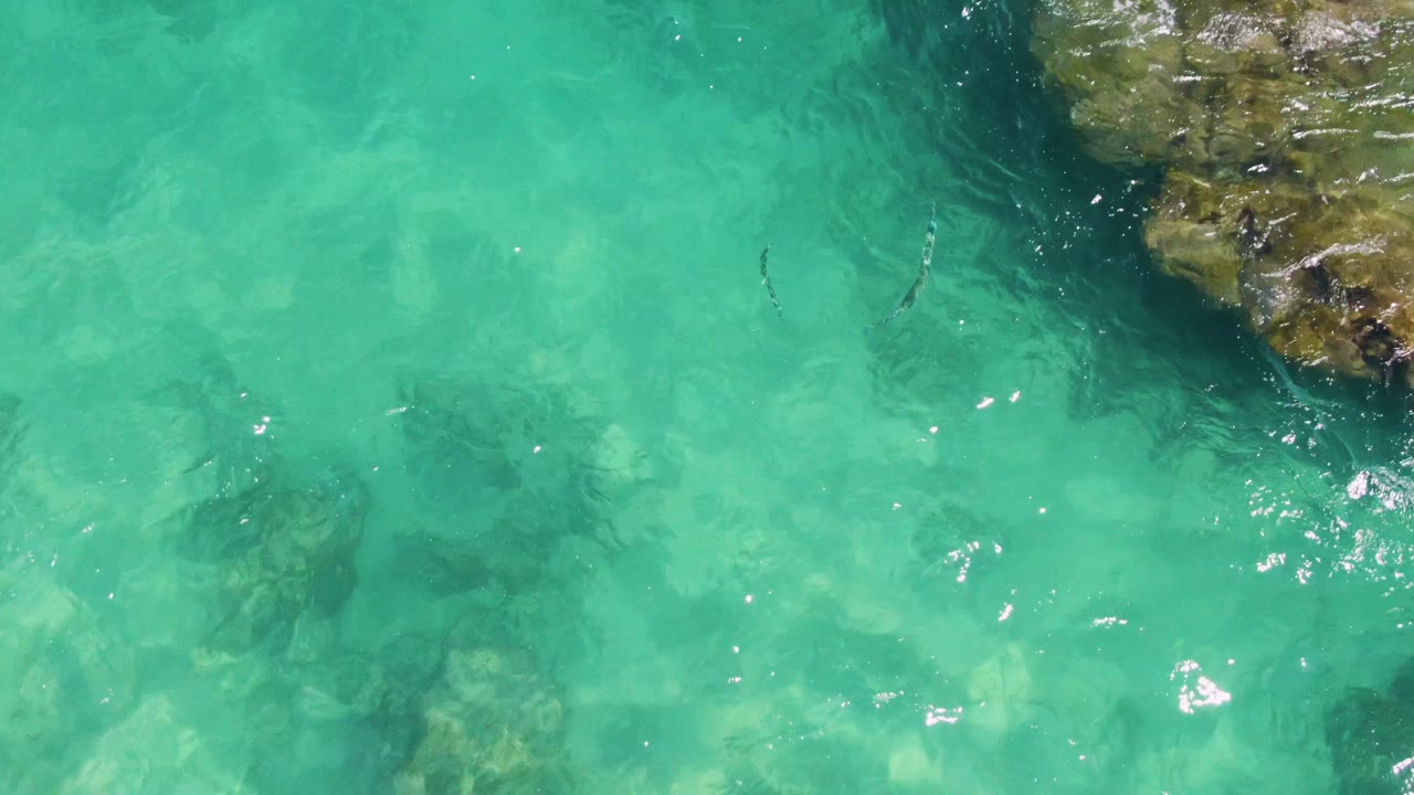 Turquoise water over submerged rocks beside a rocky outcrop