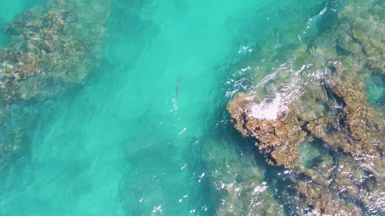 Overhead view of turquoise water at Buzzards Beach, Baja California Sur, with submerged rocks at left and center and no visible people.