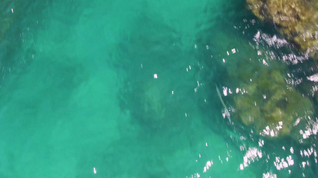 Clear turquoise water with submerged rocks and bright surface reflections.