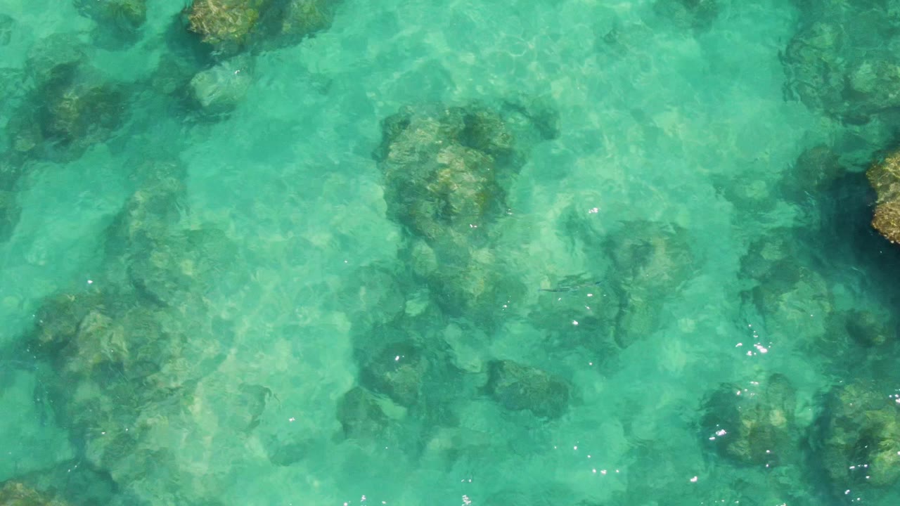 Turquoise shallow water at Buzzards Beach reveals darker seabed patches and scattered rocks under a lightly rippled surface, with no swimmers, boats, or people visible.