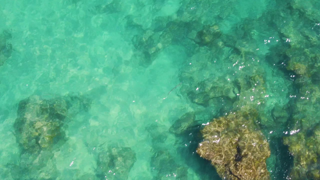 Large submerged rock under clear turquoise water with ripples and sunlight reflections.