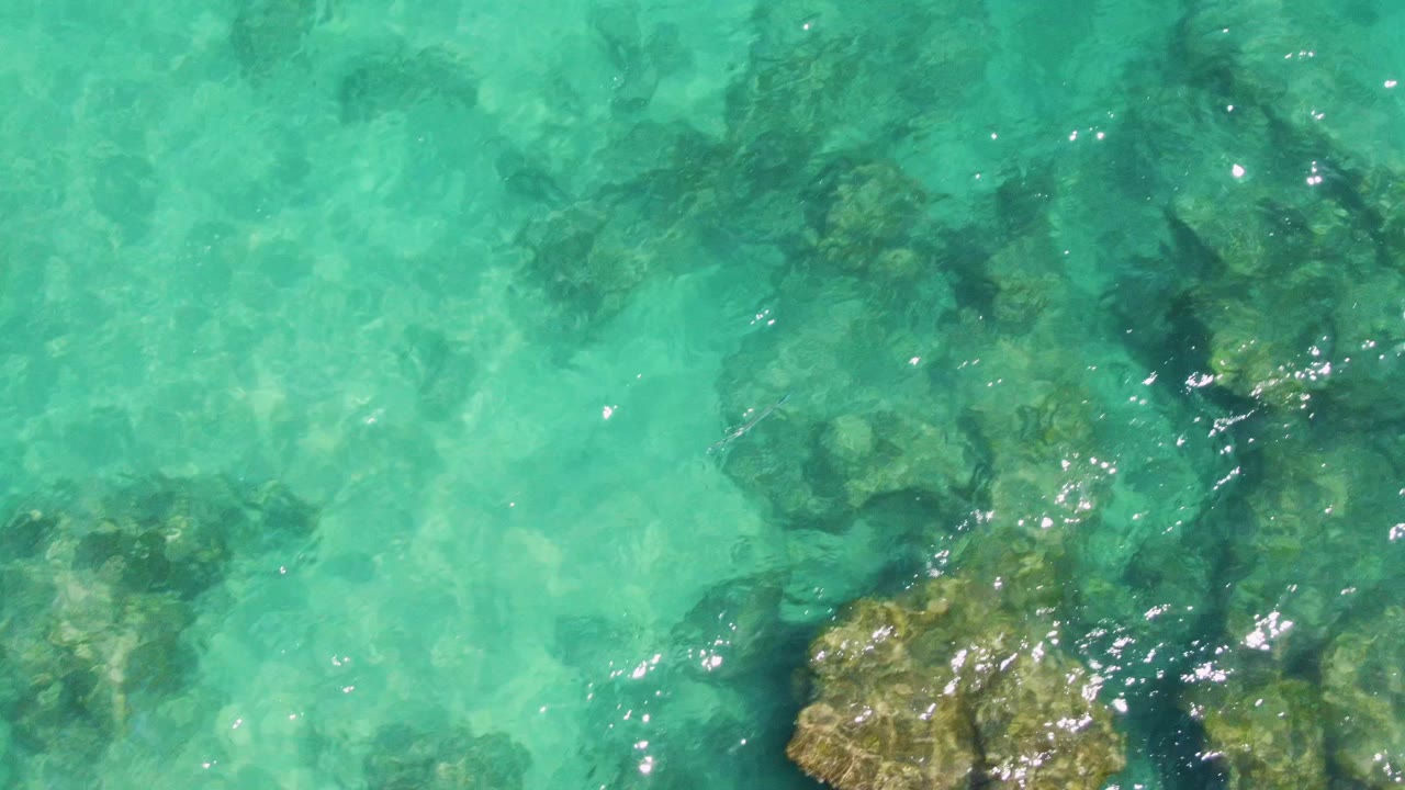 Scattered underwater rocks show through bright turquoise water at Buzzards Beach, Baja California Sur, with small reflective highlights and no visible people.