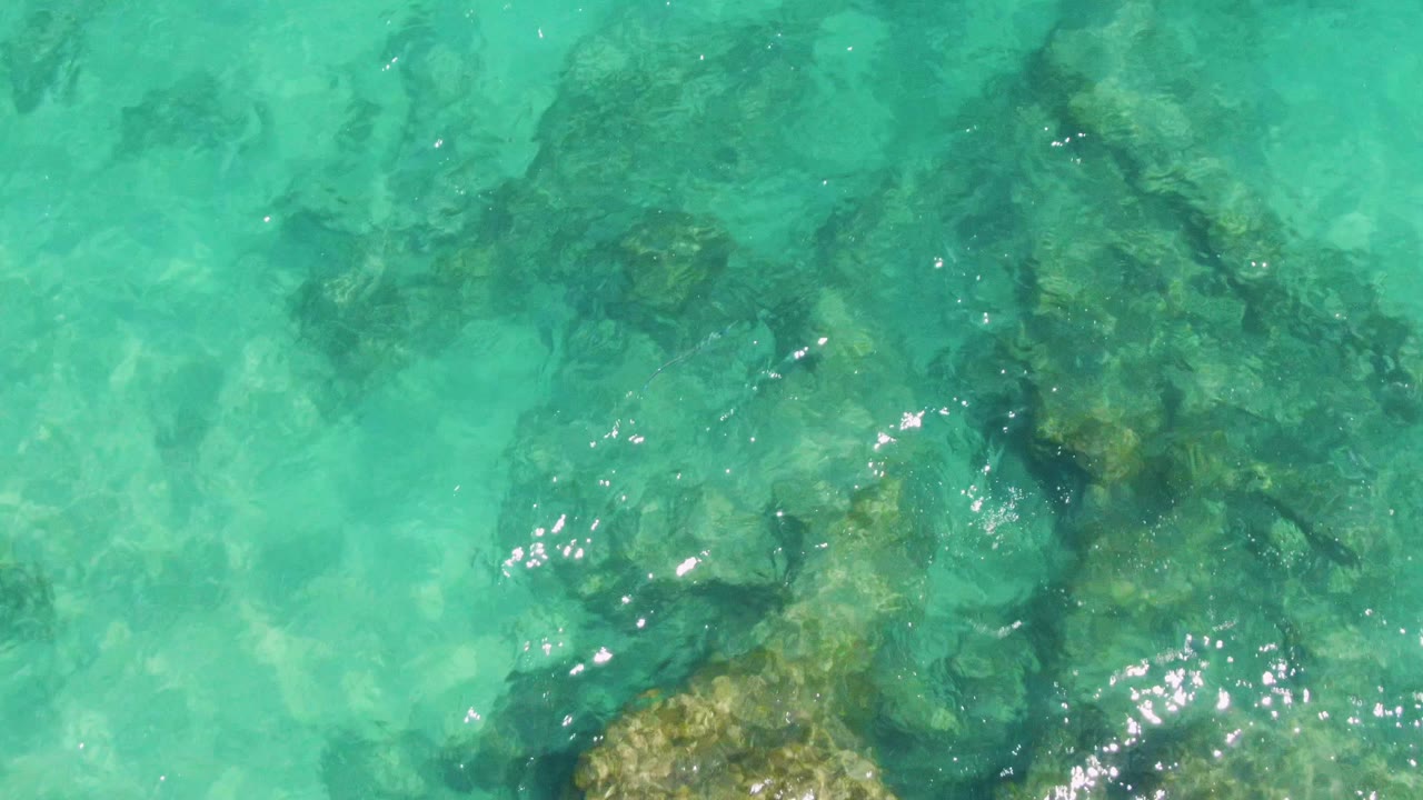 Turquoise shallow water with submerged rocks and sun glints.