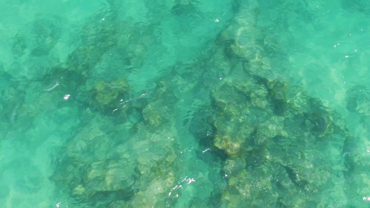 Aerial detail of turquoise water at Buzzards Beach, Baja California Sur, with submerged rocks spread across the lower frame and a smoother water patch above, no visible people.