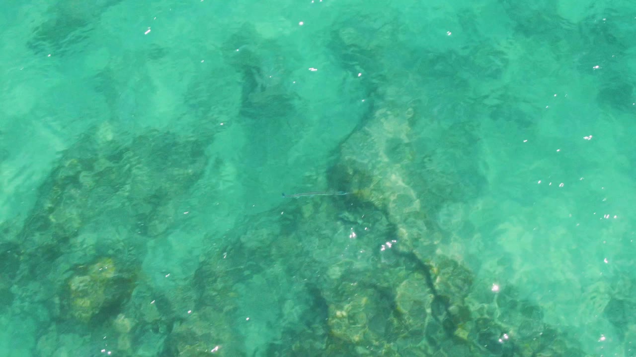 Overhead shallow ocean water at Buzzards Beach shows softer ripples, partially obscured rocks, green-blue color, and no visible people.