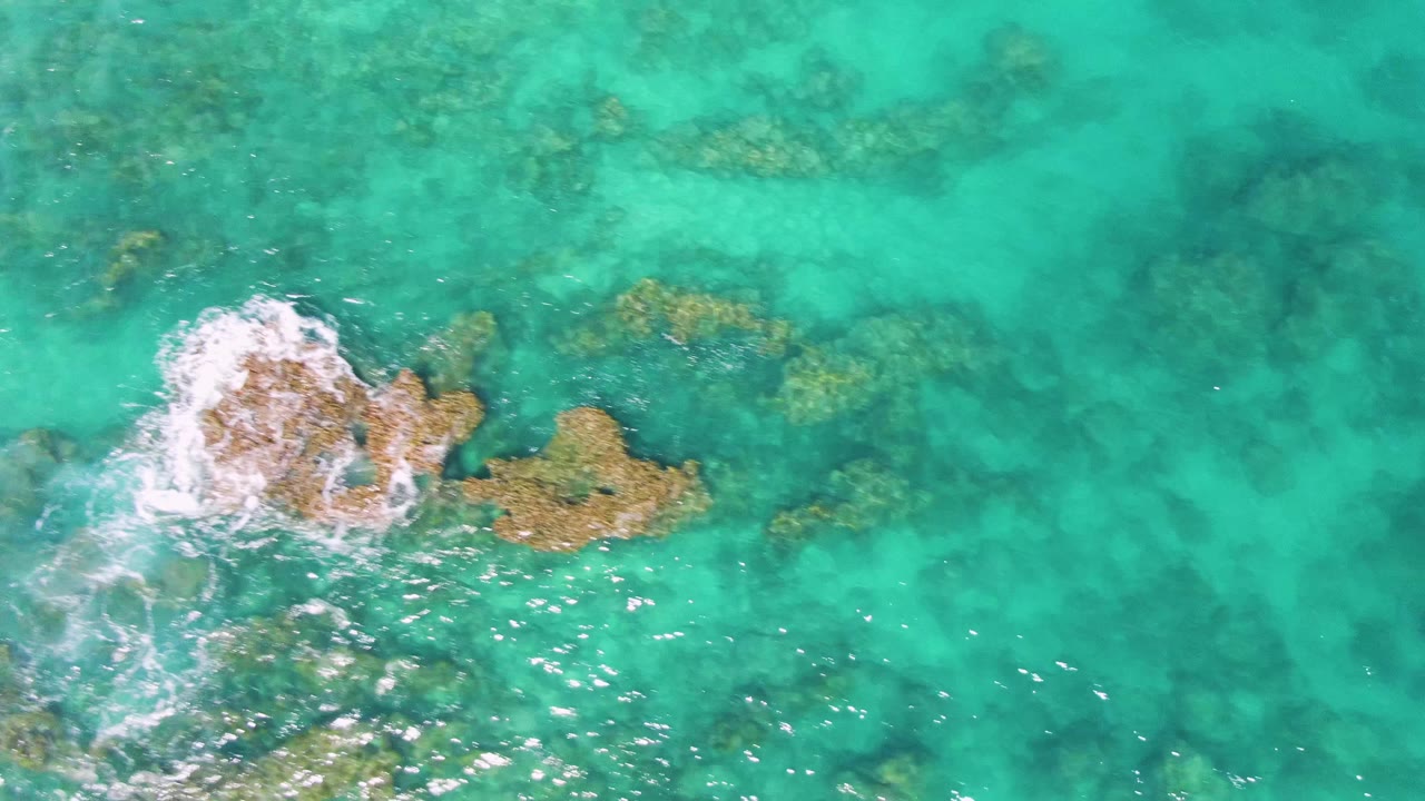Turquoise water with foam breaking over submerged rocks.