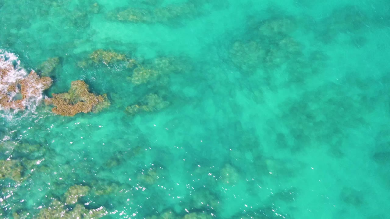 Aerial view at Buzzards Beach with the foamy rock area near the upper left, scattered underwater formations across turquoise water, and no visible people.