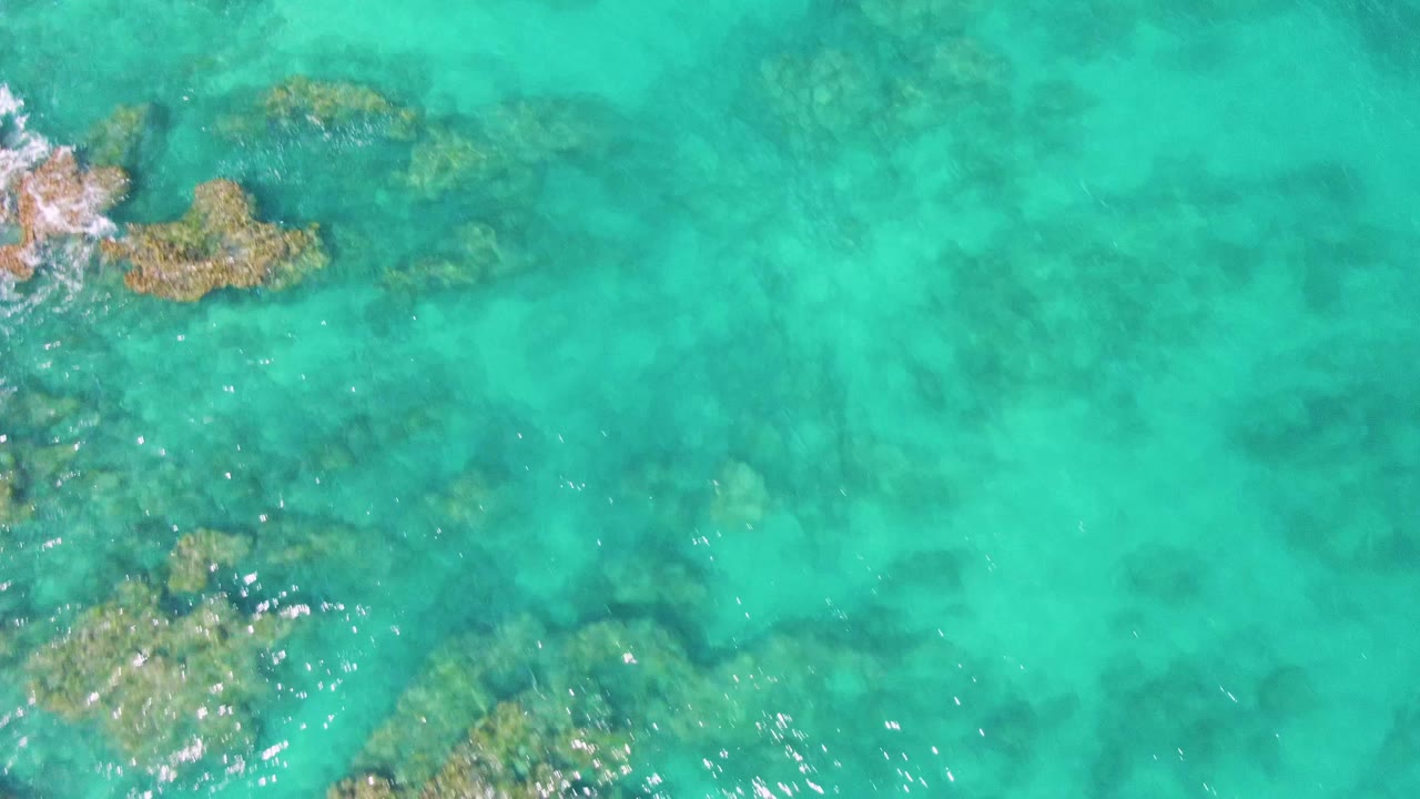 Buzzards Beach turquoise water fills the frame with submerged rock patches along the left and lower areas, faint wave texture, and no visible people.