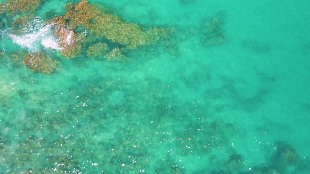 Turquoise water over submerged rocks with foam at the upper left