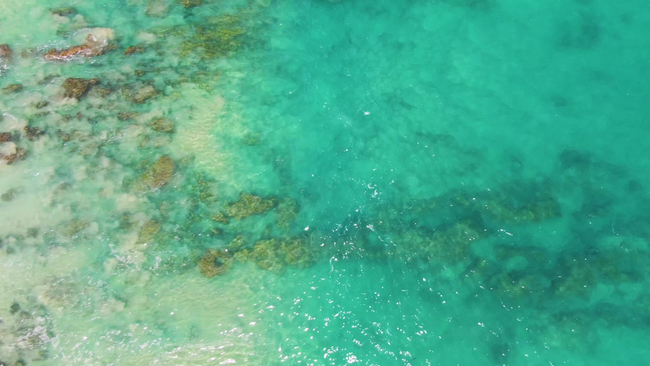 Turquoise ocean water over pale sand and submerged rocks.