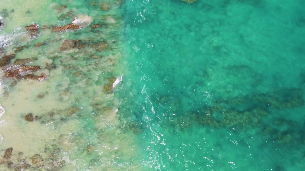 A thin patch of white foam appears near the rocky left edge while turquoise water fills the right side at Buzzards Beach, Baja California Sur, with no visible people.