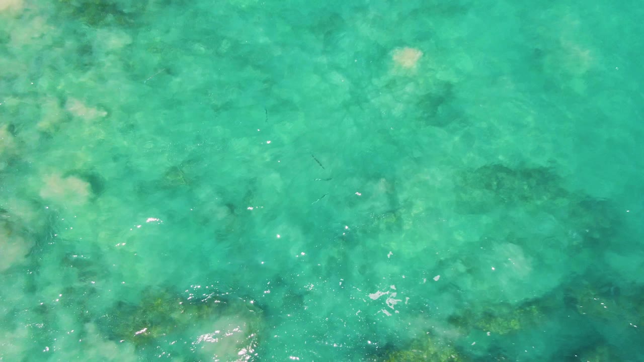 Clear turquoise water over a shallow seabed with submerged dark patches.