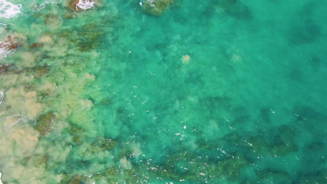 Clear green-blue shallow water over rocks and sand with foam along the left side.