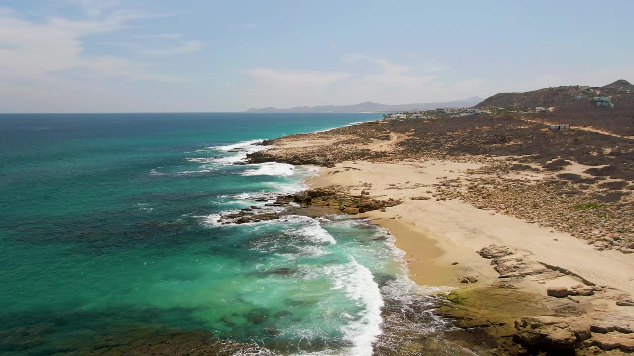 Third frame over Buzzards Beach captures a broader band of white surf crossing the rocky shoreline, with turquoise water in front, sand to the right, and no visible people.