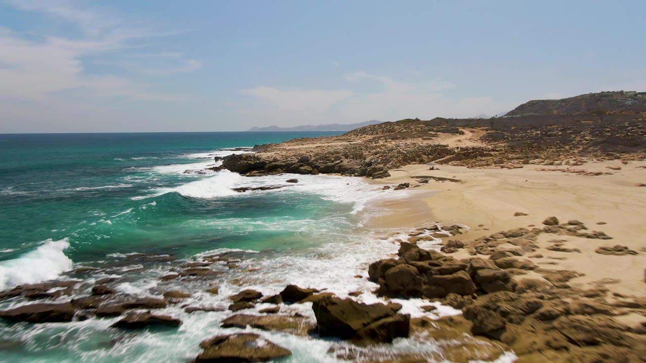 Turquoise waves breaking over rocks beside a sandy beach