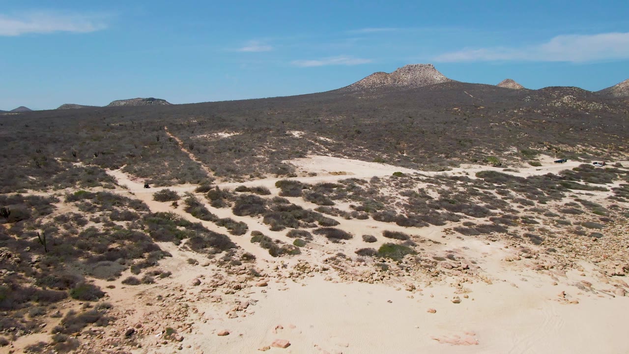 Wide desert scrub with sandy dirt tracks and distant rocky hills.