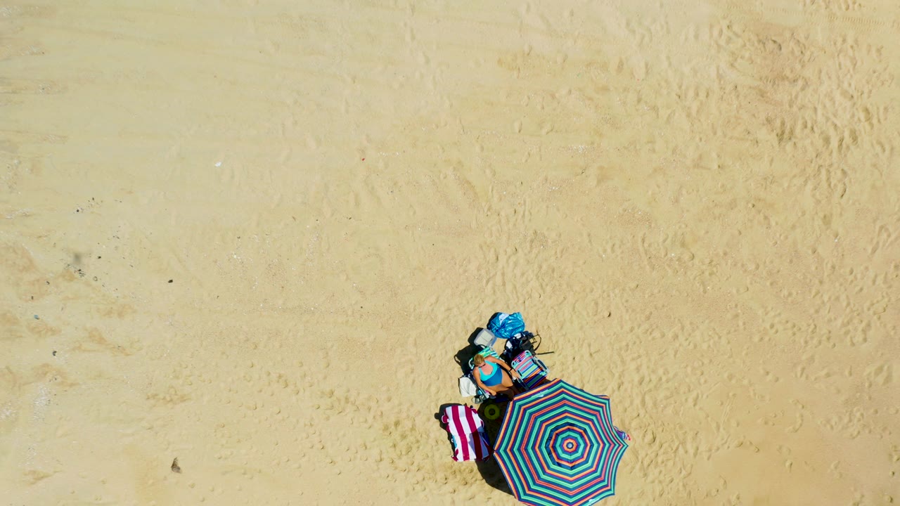 Overhead view of striped umbrella and towel on pale sand