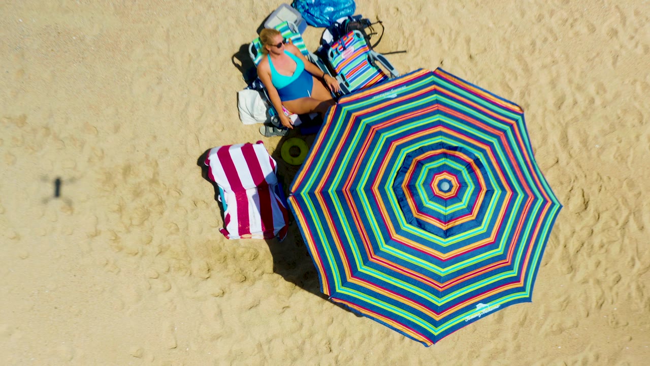 Top-down beach setup with a woman, umbrella, towel, chair, and bags.
