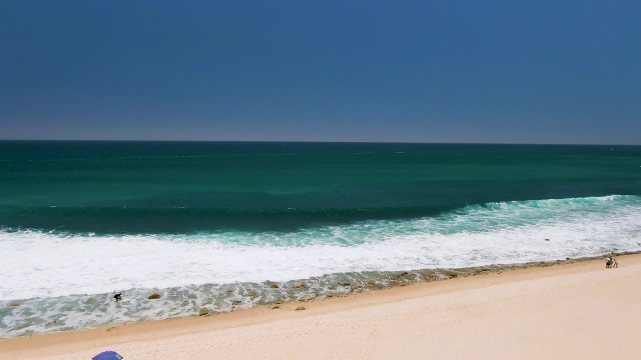 Breaking waves approach sand with a small person visible near the surf.
